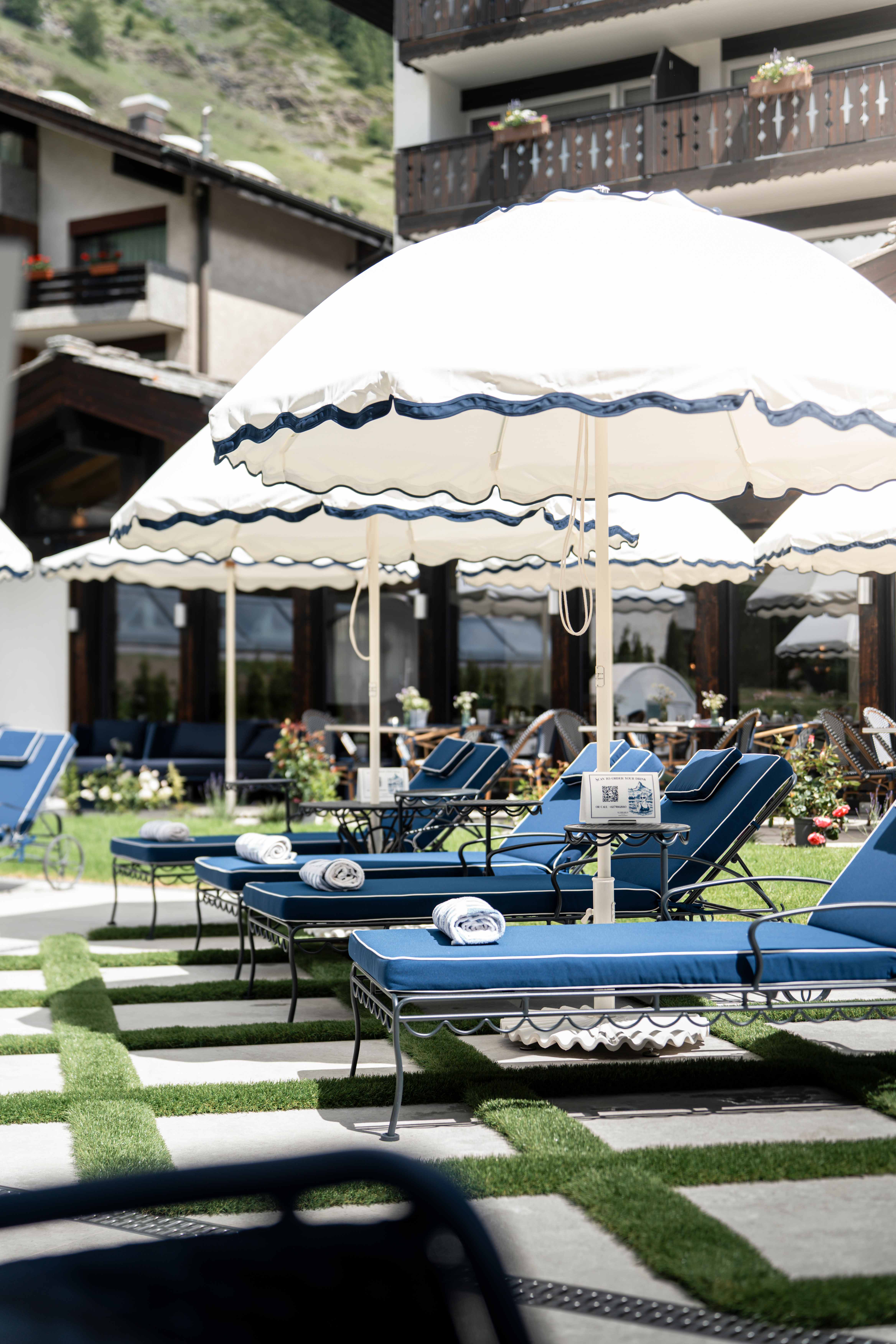 Blaue Liegestühle mit weiss-blauen Sonnenschirmen auf der Poolterrasse